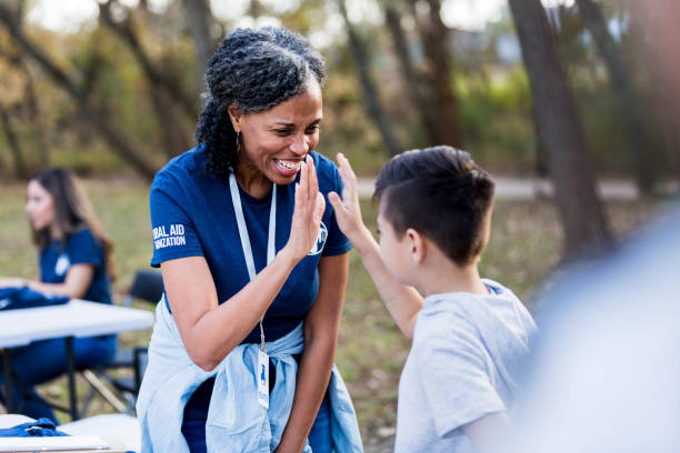 The mature adult female volunteer gives the young boy a high five for volunteering to clean up the community park.